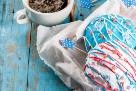 Food for independence day. 4th of July. Festive breakfast: American donuts with glaze in colors of USA flag blue, red, white. Cup of coffee. On light blue old rustic wooden table. copy spaceの写真素材