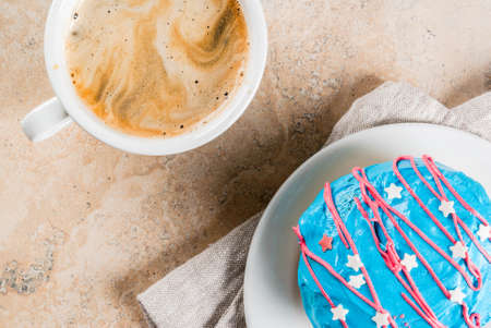 Food for independence day. 4th of July. Festive breakfast: traditional American donuts with glaze in colors of USA flag blue, red, white. Cup of coffee. On light stone table. Top view copy spaceの写真素材