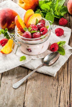 Summer healthy breakfast. Overnight oatmeal in a jar, granola, nuts, fresh raspberries and peach, decorated with mint leaves. On the old rustic wooden table. Copy spaceの写真素材