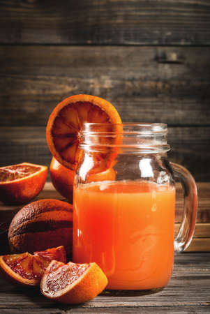 Refreshing summer drink. Juice from red Sicilian oranges. On a rustic wooden table, with whole and cut oranges. Copy spaceの写真素材
