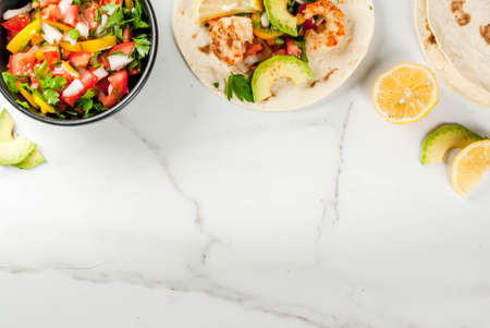 Seafood. Mexican food. Tortilla tacos with traditional homemade salsa salad, parsley, fresh lemon, avocado and grilled shrimp pawns. On a white marble background. Top view copy spaceの写真素材