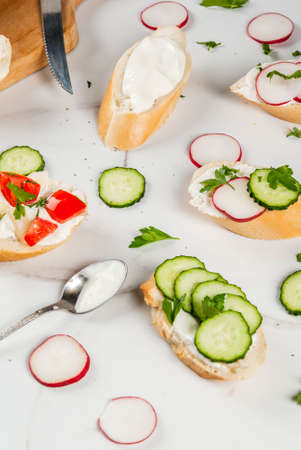 Healthy food. Spring, summer snacks. Sandwiches toast with homemade cream cheese and fresh vegetables - radish, cucumber, tomatoes, onion, pepper. On a white marble table.の写真素材
