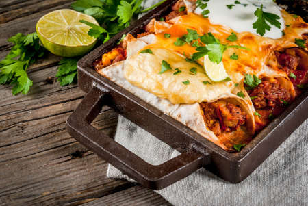 Mexican food. Cuisine of South America. Traditional dish of spicy beef enchiladas with corn, beans, tomato. On a baking tray, on old rustic wooden background. Copy spaceの写真素材