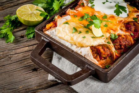 Mexican food. Cuisine of South America. Traditional dish of spicy beef enchiladas with corn, beans, tomato. On a baking tray, on old rustic wooden background. Copy space