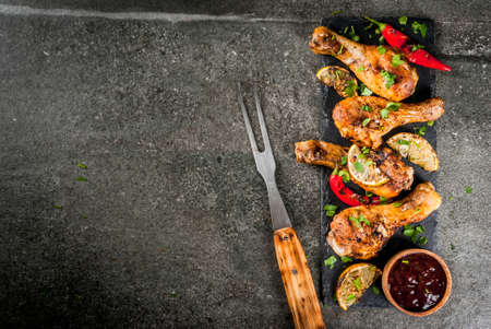 Summer food. Ideas for barbecue, grill party. Chicken legs, wings grilled, fried on fire. With hot chili pepper, lemon and bbq sauce. Dark stone table, Copy space top viewの写真素材