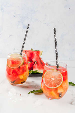 Summer drinks and cocktails. Lemonade, homemade sangria with fresh watermelon, lime, mint and pineapple. In two glasses,  on a white marble table. Copy spaceの写真素材