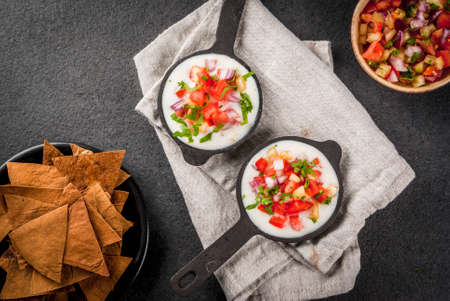 Mexican, LatinAmerican cuisine. Queso blanco recipe - cream cheese, cream, fresh stewed vegetables tomatoes, onions, peppers,  herbs. With Baked Tortilla Chips, black stone table. Top view copy spaceの写真素材