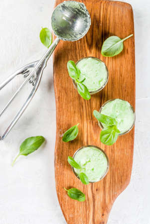 Summer desserts. Vegan food. Basil ice cream in serving glasses, decorated with fresh basil leaves. On a wooden cutting board, on a stone white table. Copy space top viewの写真素材