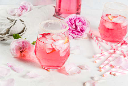 Summer refreshment drinks. Light pink rose cocktail, with rose wine, tea rose petals, lemon. On a white stone concrete table. With striped pink tubules, petals and rose flowers. Copy spaceの写真素材