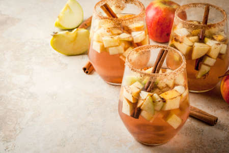 Autumn and winter drinks. Warm apple sangria, apple cider with pieces of fruit, cinnamon, spices, sugar. In glasses, on a stone beige table. With the ingredients. Copy spaceの写真素材