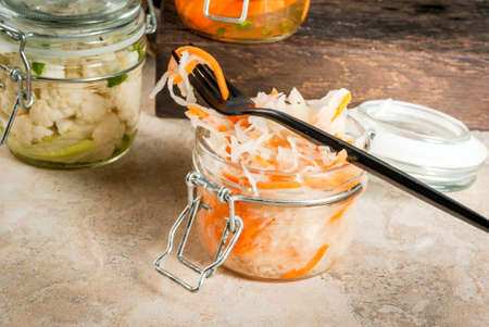 Concept of a fermented meal. Home canned food and billets. Vegan food. Vegetables. Cans of canned salsa, sauerkraut, marinated carrots, kimchi and cauliflower broccoli. Home kitchen table. copy spaceの写真素材