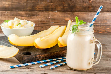 Smoothie of yogurt, raw organic yellow melon, flax seeds and mint. With striped straws, in mason jar, wooden rustic table, copy spaceの写真素材
