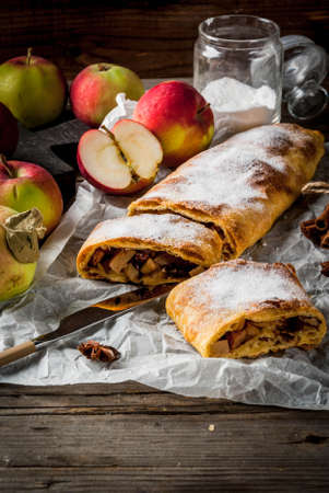 Home autumn, summer baking, puff pastries. Apple strudel with nuts, raisins, cinnamon and powdered sugar. On a wooden old rustic table. Sliced, with ingredients. Copy spaceの写真素材