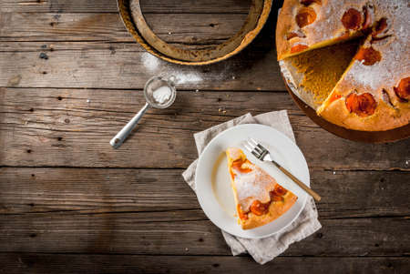 Homemade autumn and summer baked pastries. Sponge cake with apricots. Cut into pieces, plate, fork. On the stand. On the old wooden rustic table. Copy space top viewの写真素材