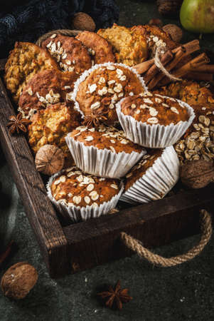 Autumn winter pastries. Vegan food. Healthy homemade baking cookies, muffins with nuts, apples, oat flakes. Cozy home atmosphere, warm blanket, ingredients for baking. Dark stone table. Copy spaceの写真素材
