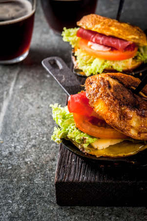 Mexican Tortilla de patatas rellena de jamón serrano - casserole with potato, eggs, sandwich with meat, lettuce, cheese, tomatoes. In portioned frying pans, with beer, black stone table.  Copy spaceの写真素材