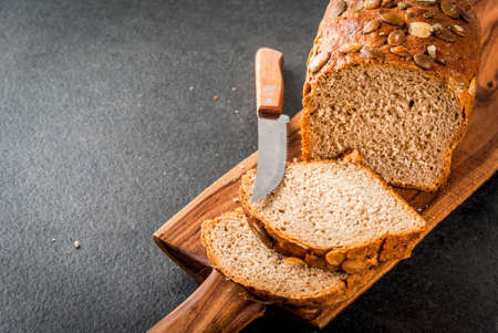 Freshly baked homemade organic multi-grain bread with pumpkin seeds on a cutting board on a black stone table. Copy spaceの写真素材