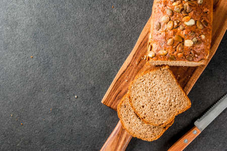 Freshly baked homemade organic multi-grain bread with pumpkin seeds on a cutting board on a black...