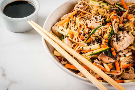 Traditional Asian food. Lunch stirfry: rice noodles, zucchini, carrots, bamboo, mushrooms, pork (beef), soy sauce and black sesame. With soy sauce, chopsticks. Copy spaceの写真素材