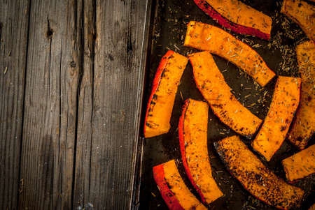 Traditional autumn dishes from pumpkin. Fried baked on grill pumpkin with spices, olive oil, herbs. On a baking sheet, on a rustic wooden old table. Top view copy spaceの写真素材