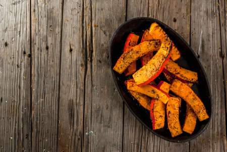 Traditional autumn dishes from pumpkin. Fried baked on grill pumpkin with spices, olive oil, herbs. On a baking sheet, on a rustic wooden old table. Top view copy spaceの写真素材