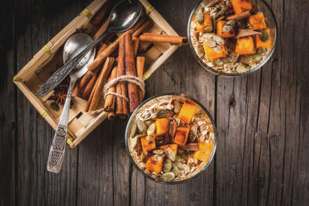Traditional autumn dishes, spicy pumpkin pie overnight oatmeal with cinnamon, anise and maple syrup. In portioned glasses, on wooden old rustic table. Copy space top viewの写真素材