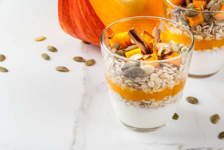 Traditional autumn dishes, spicy pumpkin pie overnight oatmeal with cinnamon, anise and maple syrup. In portioned glasses, on white marble table. Copy spaceの写真素材