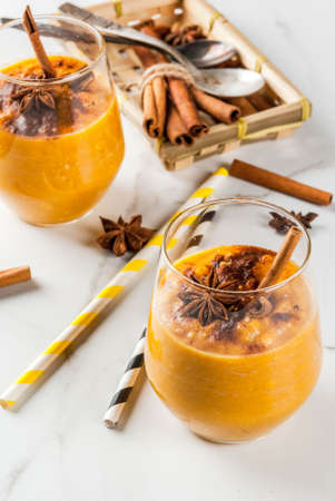 Traditional autumn dishes, spicy pumpkin pie smoothie with cinnamon, anise and oatmeal. In portioned glasses, on white marble table. Copy spaceの写真素材