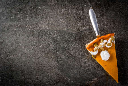 Traditional autumn dishes. Halloween, Thanksgiving. One piece of spicy pumpkin pie with whipped cream & pumpkin seeds on black stone table. Copy space top viewの写真素材