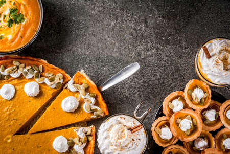 Set of traditional autumn food. Halloween, Thanksgiving. Spicy pumpkin latte, pumpkin pie and tartalets with whipped cream and pumpkin seeds, pumpkin soup, on black stone table. Copy space top viewの写真素材