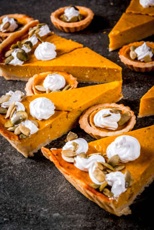 Traditional autumn dishes. Halloween, Thanksgiving. Set of spicy pumpkin pie and pumpkin tartlets with whipped cream & pumpkin seeds on black stone table. Copy spaceの写真素材