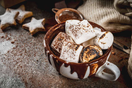 New Year and Christmas treats. Traditional sweets. A cup of hot chocolate with marshmallow fried on fire, gingerbread stars, with sweater on black stone background, copy spaceの写真素材