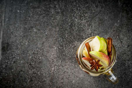 Autumn cocktail. Infused diet detox water with apples and spices - anise, cinnamon. Alcohol cocktail with apple cider. In mason jar on a black stone table. Copy space top viewの写真素材