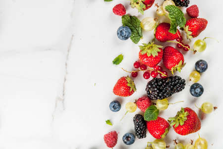 Summer fruit and berries. 6 types of raw organic farmer berries - raspberries blackberries blueberries strawberries red currants gooseberries. On white marble table. Copy space top viewの写真素材