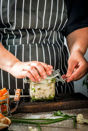 Concept of fermented meal. Canned food. Vegan food. Vegetables. Person (woman) cook fermented sauerkraut salted broccoli cauliflower. Cans with conservation sauerkraut, carrots, greens, onions.の写真素材