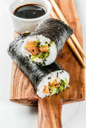 Trend hybrid food. Japanese, Asian cuisine. Sushi-burrito, sandwich with salmon, hayashi wakame, daikon, pickled ginger, red caviar. On a white marble table, with chopsticks and soy sauce. Copy spaceの写真素材