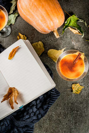 Fall and winter drinks. Thanksgiving and Halloween cocktails. Pumpkin pie margarita with cinnamon stick, on black stone table. Cozy home, with autumn leaves, plaid, pumpkin, book, copy space top viewの写真素材