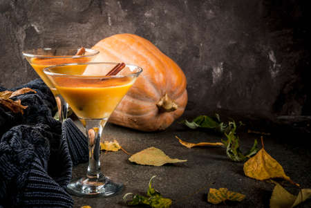 Fall and winter drinks. Thanksgiving and Halloween cocktails. Pumpkin pie margarita with cinnamon stick, on black stone table. Cozy home, with autumn leaves, plaid, pumpkin, copy spaceの写真素材