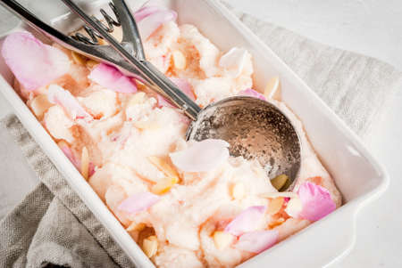 Summer refreshing desserts. Vegan diet food. Ice cream with rose petals and slices of almond, in white serving bowl, on a white concrete table. Copy space close viewの写真素材