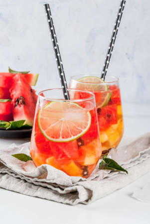 Summer drinks and cocktails. Lemonade, homemade sangria with fresh watermelon, lime, mint and pineapple. In two glasses,  on a white marble table. Copy spaceの写真素材