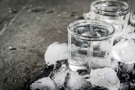 Alcohol and cocktails. Three glasses of vodka on a slate tray, with ice. On a black stone table, Copy spaceの写真素材