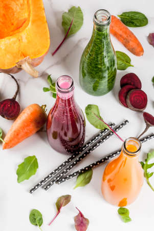 Vegan diet food. Selection colorful fresh organic smoothies drinks with autumn vegetables: beetroot, pumpkin, carrot, leafy vegetables. In bottles, white table. Copy space top viewの写真素材