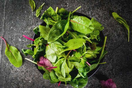 Bowl with fresh green organic leaves, baby spinach lettuce, on a black stone table, copy space top...