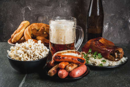 Selection of traditional German food Oktoberfest. Beer, baked pork shank, popcorn, assortment of different sausages, homemade bretzels. On a black stone background copy spaceの写真素材