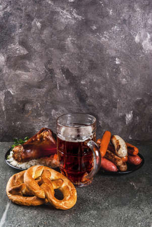 Selection of traditional German food Oktoberfest. Beer, baked pork shank, popcorn, assortment of different sausages, homemade bretzels. On a black stone background copy spaceの写真素材