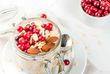 Recipe for a healthy winter breakfast, ideas for Christmas morning. Overnight oatmeal with almonds, cranberries, sugar. On a white marble table. copy spaceの写真素材