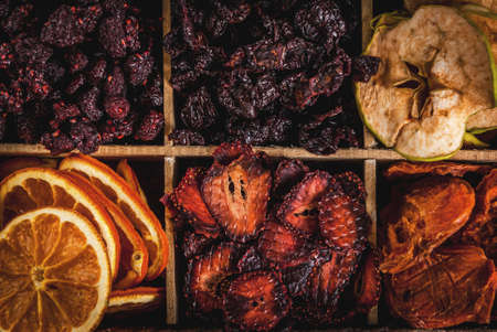 Homemade dried berries and fruits, harvest for the winter: apricots, apples, strawberries, raspberries, cherries, oranges. In old wooden box, on black stone tableの写真素材