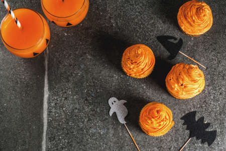 Simple idea of funny kid's treat for Halloween: pumpkin cakes with cream, with decorations in the form of holiday symbols - ghost, witch, bat. On a black background, copy spaceの写真素材