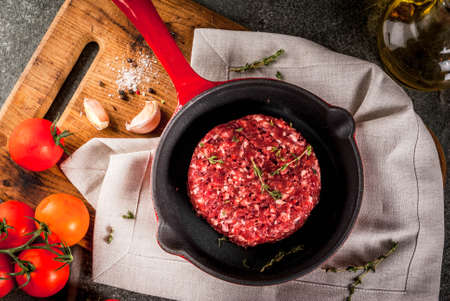 Raw organic beef meat burgers cutlets  with spices, thyme, tomatoes, olive oil in frying pan on black background, copy spaceの写真素材