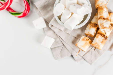 Traditional christmas sweets - candy cane, marshmallow and baked on fire marshmallow skewers on white background, copy space top viewの写真素材